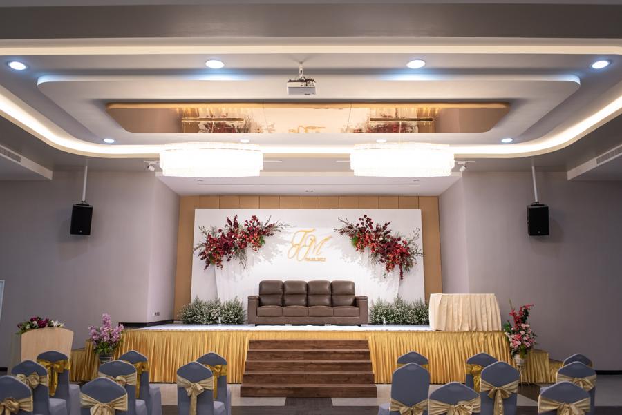 Ballroom set for a wedding with a red floral stage backdrop and gold-sashed chairs