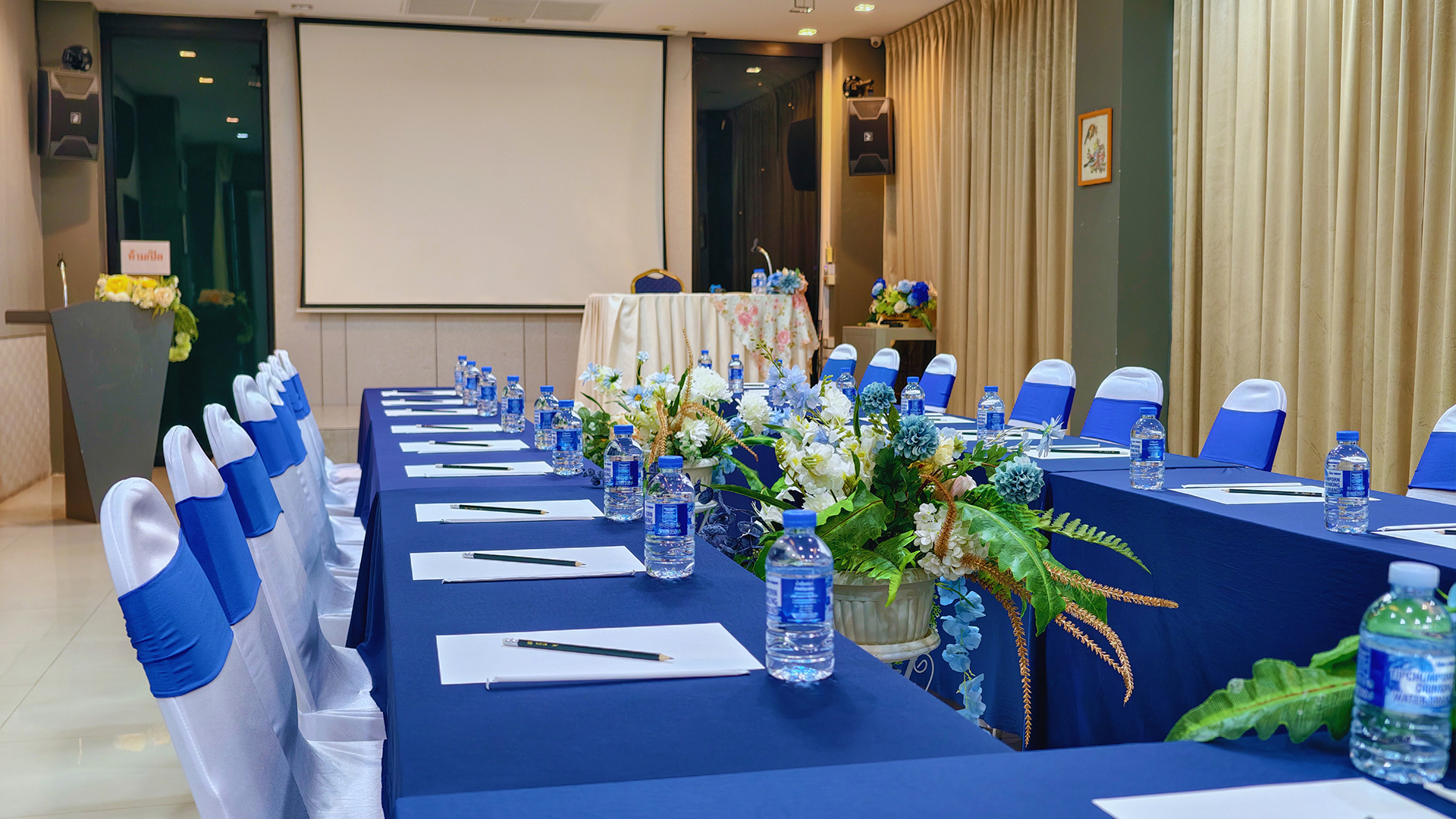 Meeting room with blue-draped tables, notepads and a projector screen