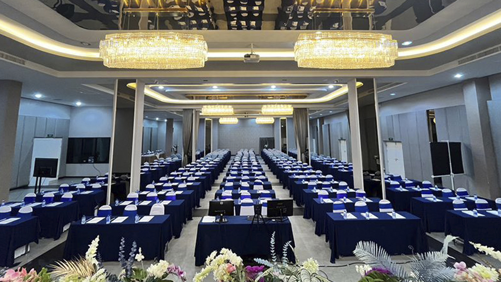 Ballroom set classroom-style with blue tables beneath crystal chandeliers