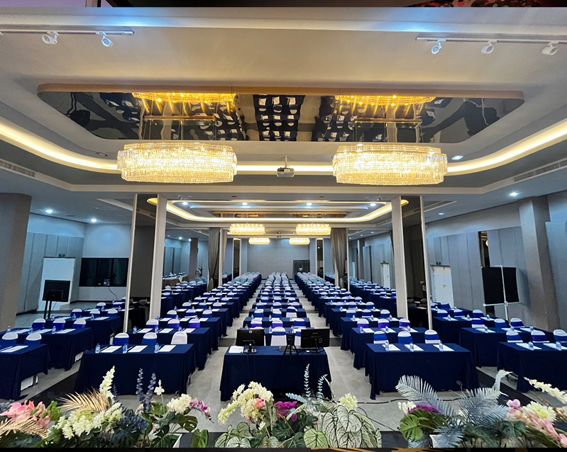 Ballroom set in classroom style with rows of blue-draped tables under crystal chandeliers