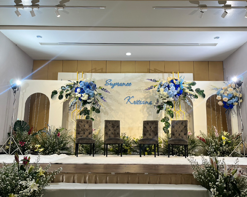 Wedding stage with a floral backdrop and four chairs for the couple and their parents